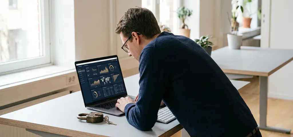 Mitarbeiter analysiert Sicherheits-Dashboard auf Laptop, physisches Schloss liegt neben der Tastatur im modernen Büro.