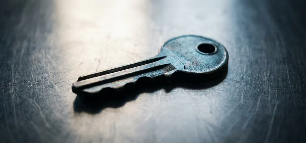 Einzelner Metallschlüssel auf gebürstetem Stahl-Schreibtisch, seitliches Diffuslicht, Makroaufnahme mit flacher Schärfentiefe.